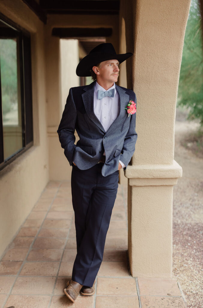 Groomsmen sharing a laugh while helping the groom with his jacket in a warm, desert inspired getting ready space.