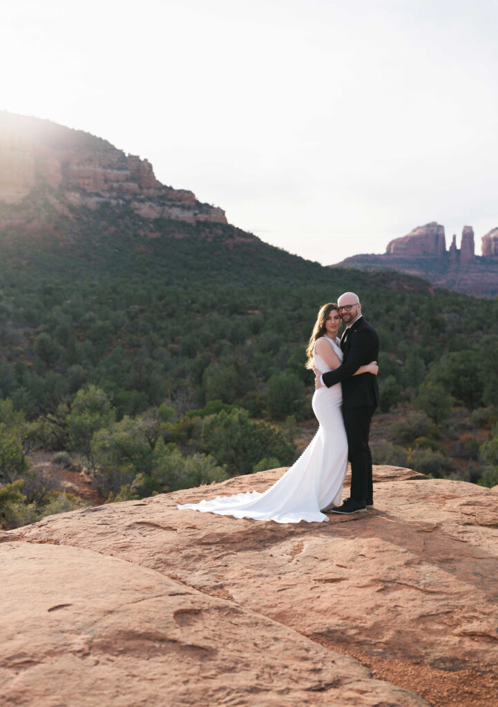 Portrait of couple embracing with Bell Rock and the Sedona red rocks behind them.