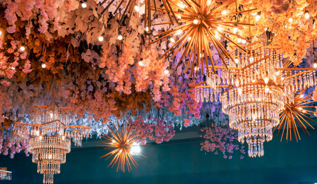 A scenic view of shiny chandeliers hanging on a ceiling surrounded by floral decorations