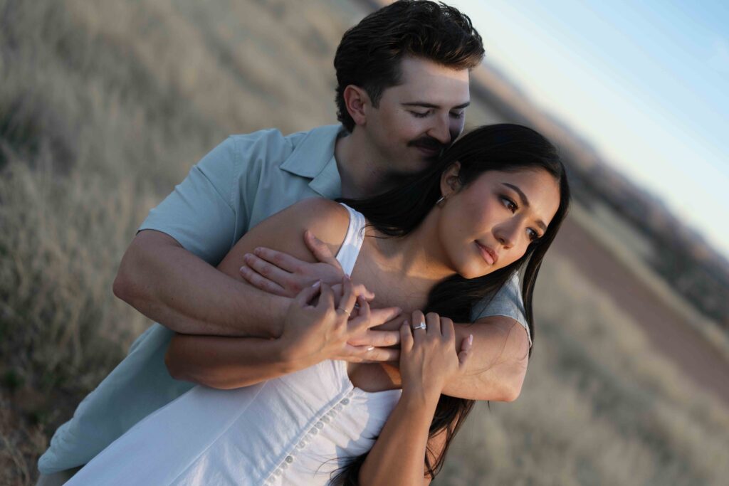 A couple holds one another looking off in the distance as they watch the sunset in an Arizona national park.  the bride is wearing a soft cotton dress and her groom is wearing a light green button up. 