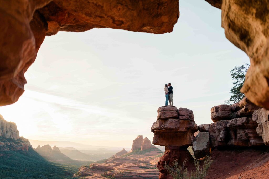 A couple stands on a rock in Papago Parks the photographer takes a portrait of them through the famous keyhole rock.