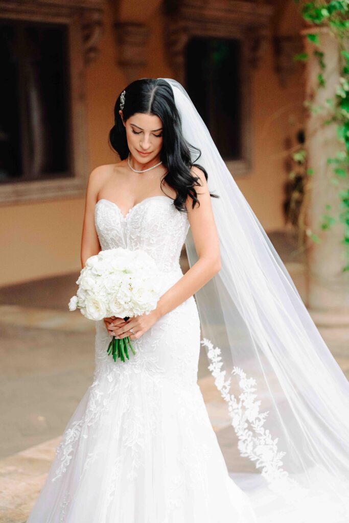 A bride stands in an elegant white lace gown in the courtyard of her Arizona Wedding venue Villa Siena. 
