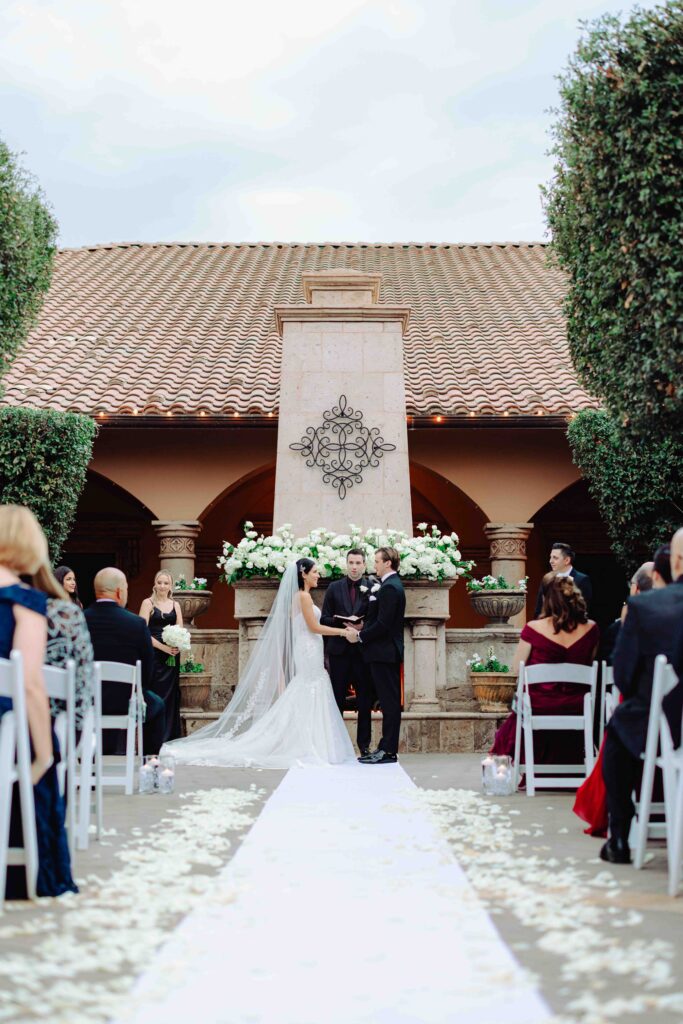 A bride and groom stand in front of an outdoor fireplace during their wedding ceremony at Villa Siena in Arizona.  