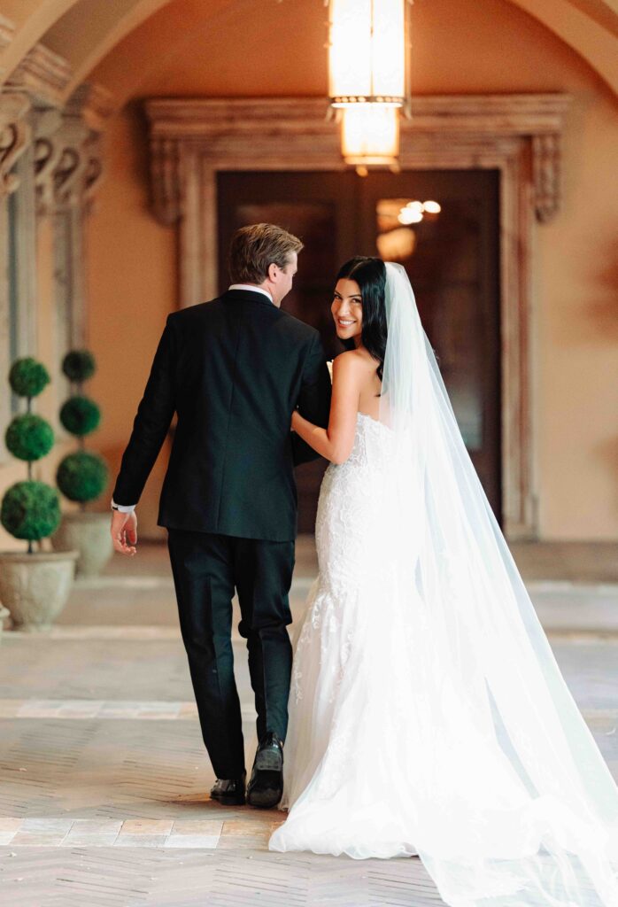 A bride and groom walk under the covered hallway along the courtyard at Villa Siena.