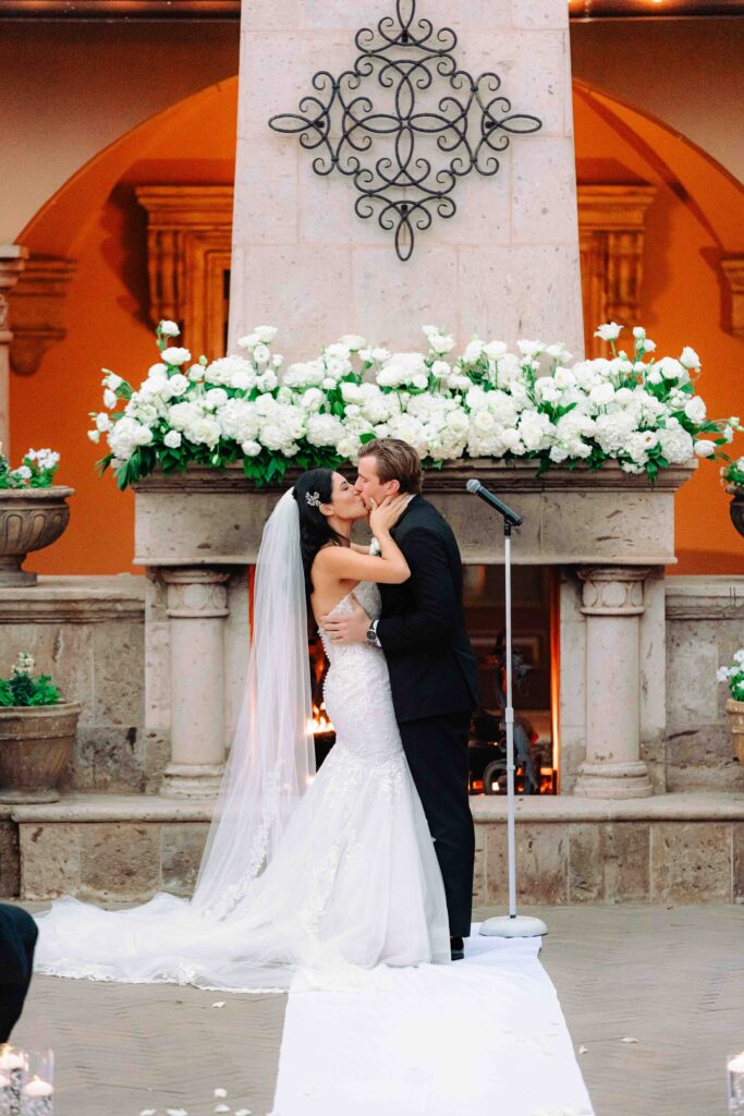 A bride and groom kiss in front of an outdoor fireplace during their wedding ceremony at Villa Siena in Arizona.  